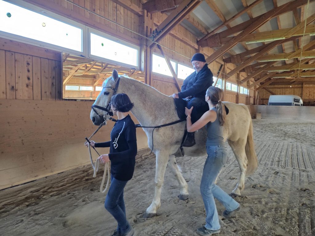 Hippotherapie: eine Person wird auf dem Pferd begleitet