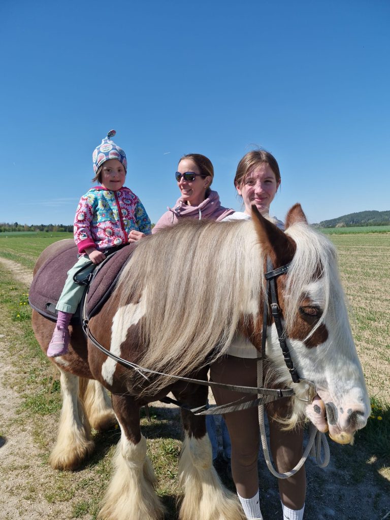 Kind beim Hippotherapie-Reiten auf dem Pferd im Freien